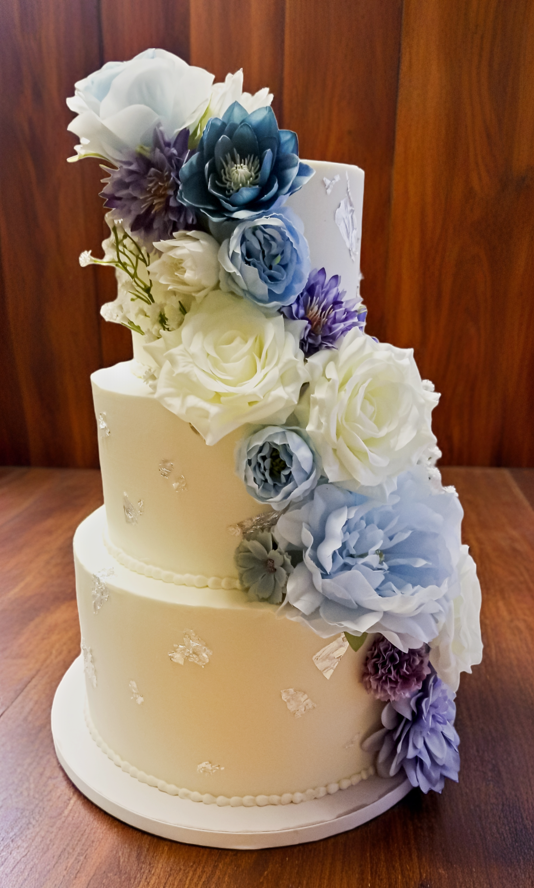 Three-tiered white wedding cake with cascading blue and white floral arrangement