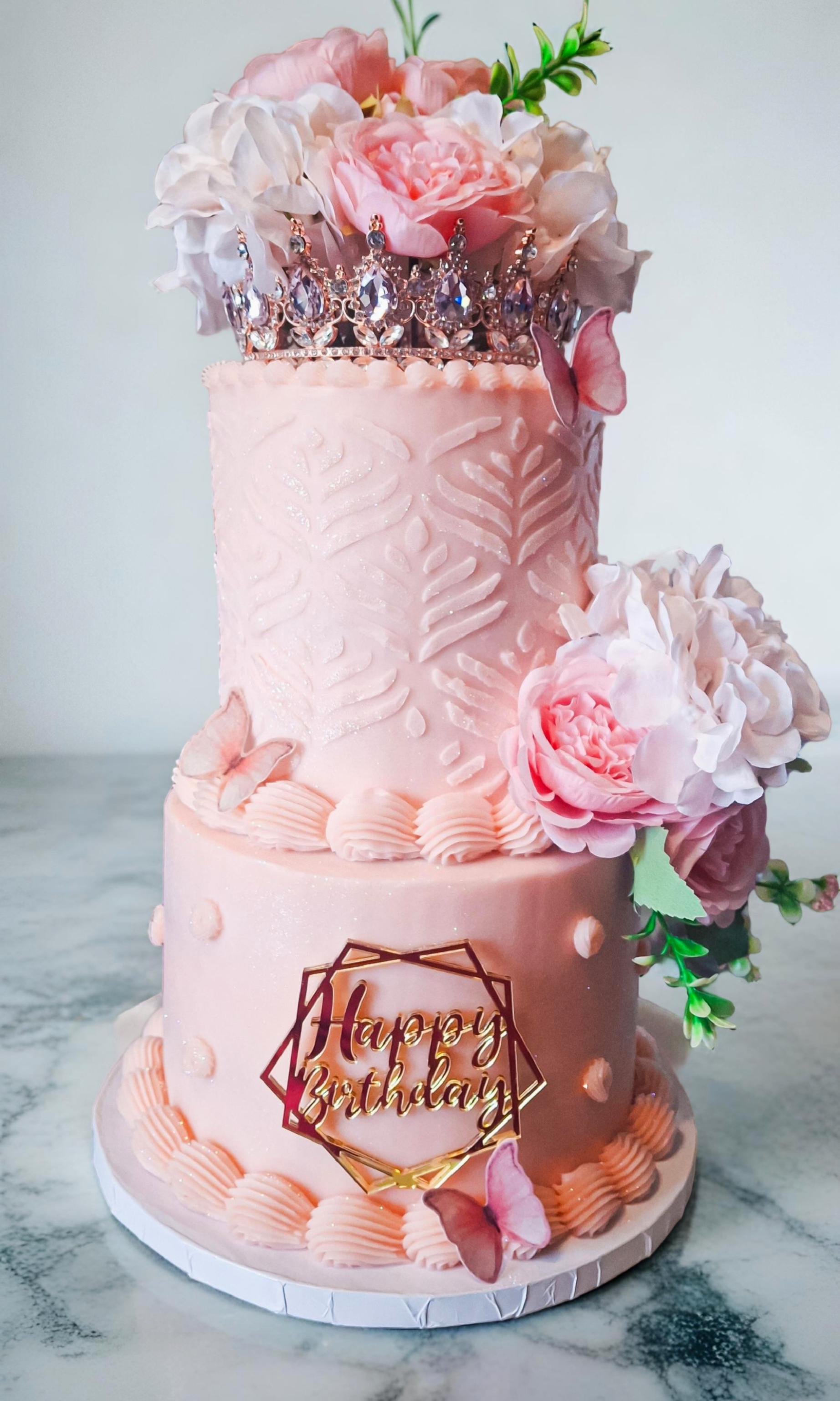 Two-tiered blush pink birthday cake with crown topper and pink peony flowers
